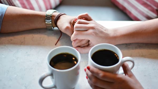 dos manos entrelazadas y dos tazas de café