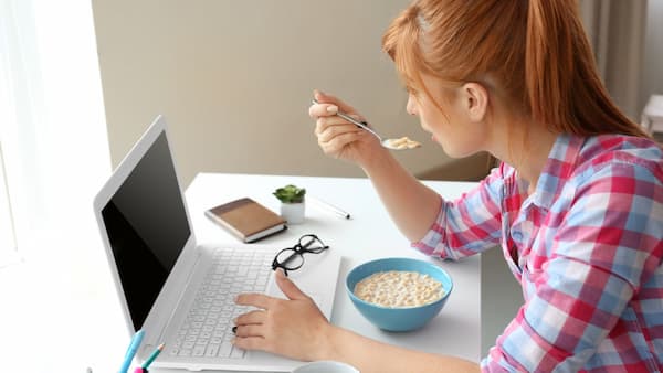 Chica comiendo un bol de cereales frente al ordenador